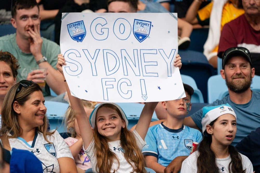 A young fan holding a Go Sydney FC sign in the stands