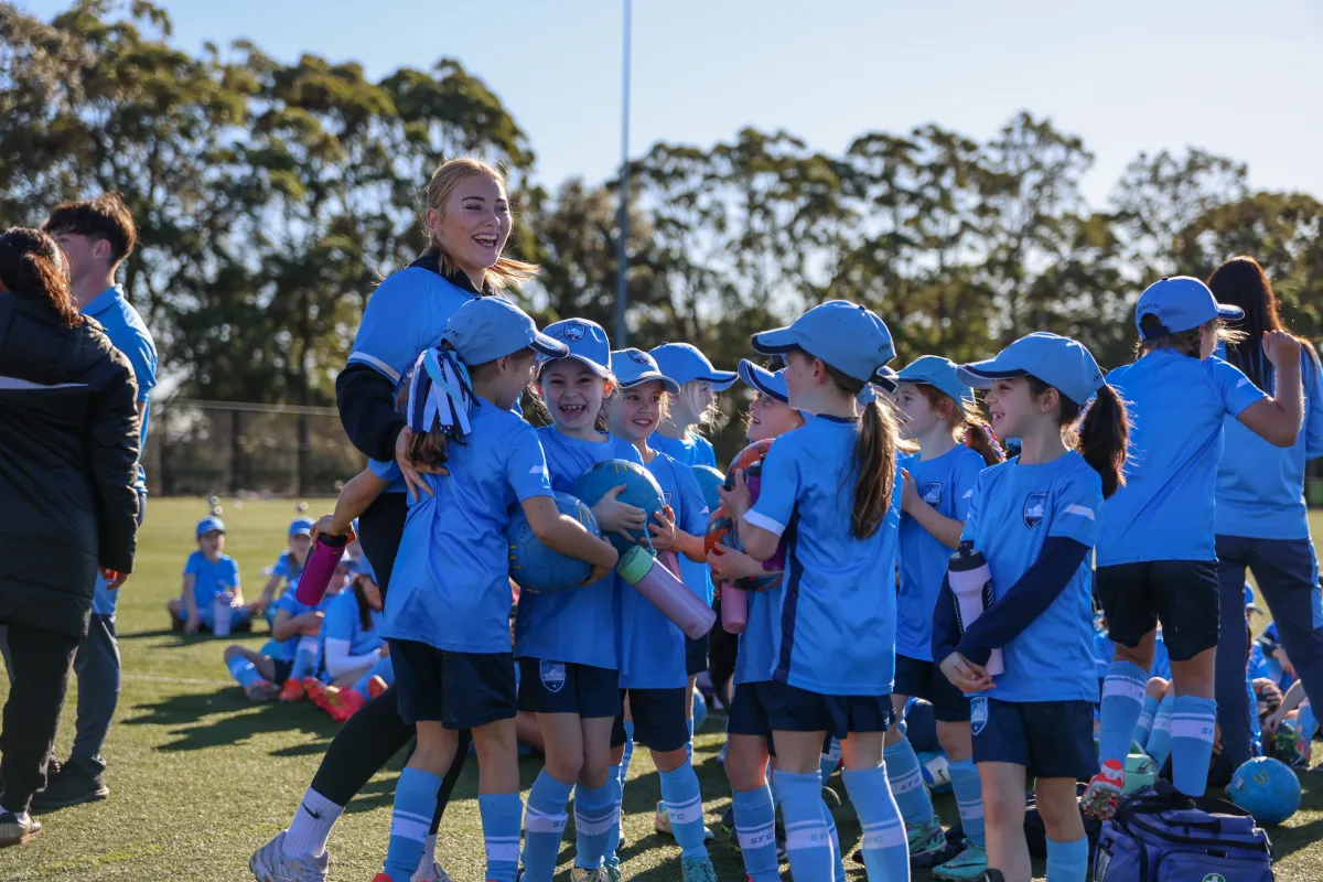Young girls in Sydney FC kit laughing with a coach at a Girls Only Holiday Clinic