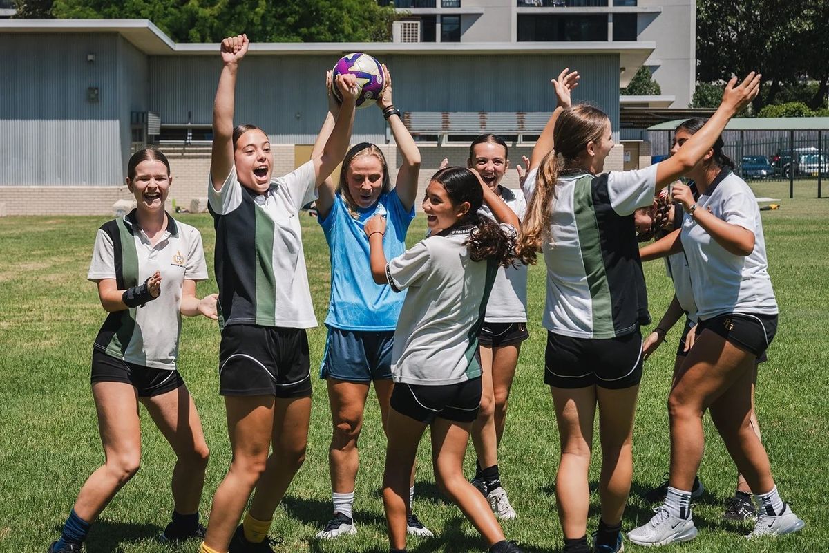Schoolgirls cheering around a Sydney FC Women player holding a ball up at a Sky’s Her Limit session
