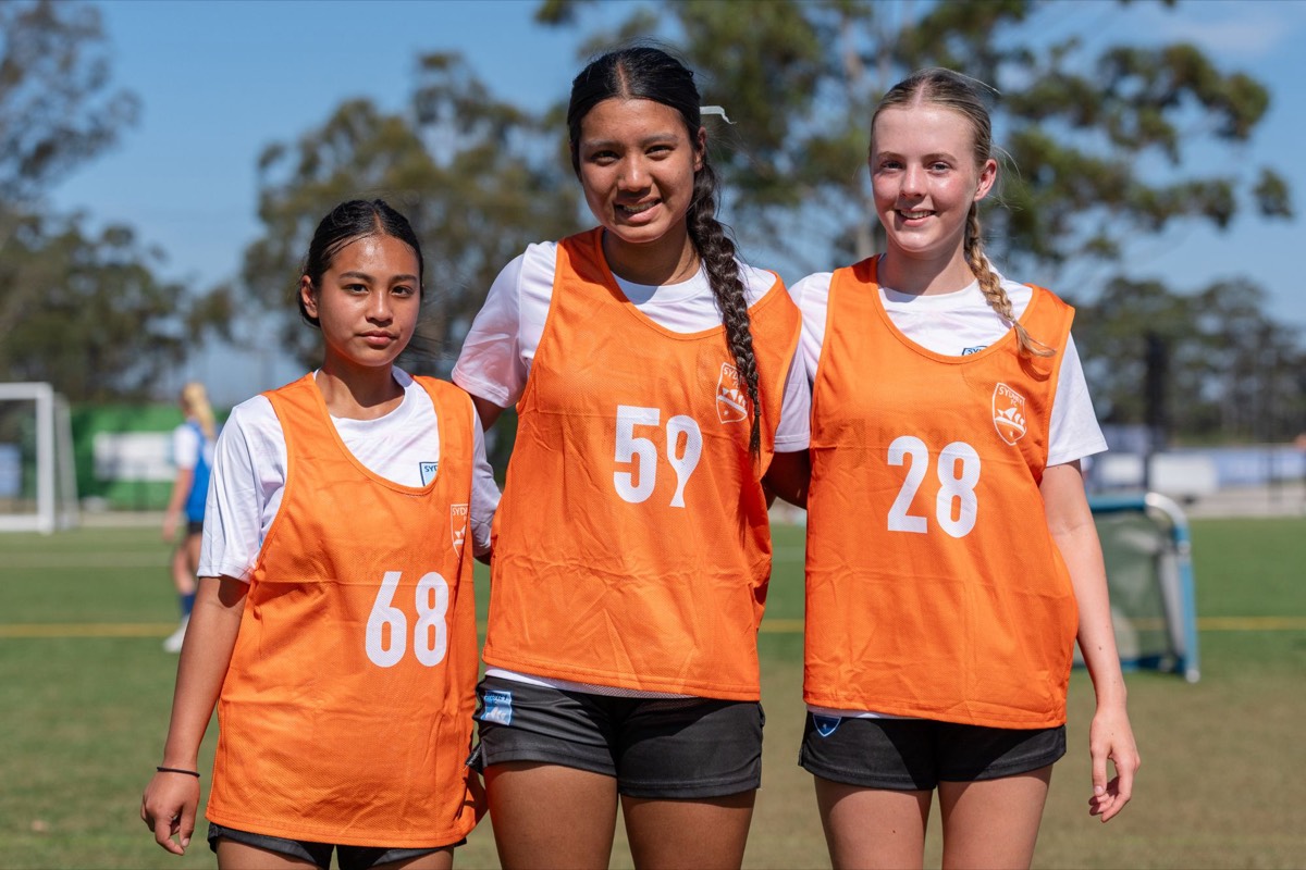 Three girls in Sydney FC training bibs smiling together at training